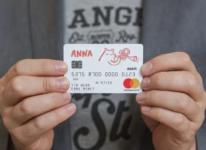 Two hands holding the white ANNA debit card, with its red line drawing of a cat blowing a horn