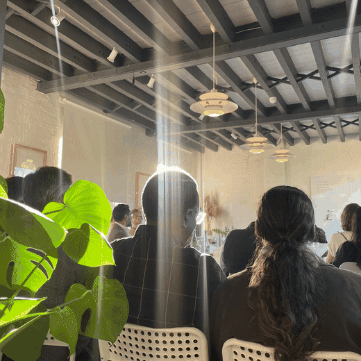 Guests seated under black beams and pendant lamps at the first Call My Bluff evening, a monstera plant in the foreground