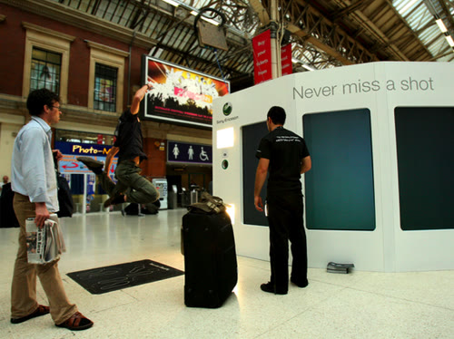A Sony Ericsson booth reading Never miss a shot in a station concourse, with a man looking at its screens and another person leaping in the background