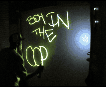 Dizzee Rascal spraying glowing green letters onto a dark glass wall