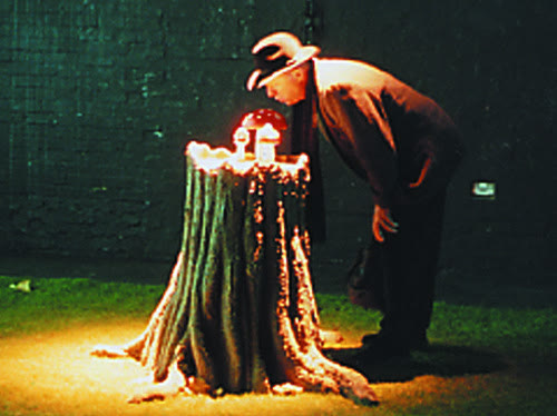 A man in a hat leans over a glowing tree stump with small lit objects on top